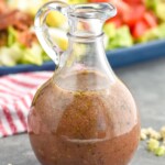 close up bottle of red wine vinaigrette with Cobb salad behind it and blue cheese and green onions around it - 8