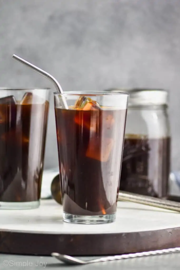 two tall tumblers full of ice and iced coffee on a tea with a mason jar full of cold coffee in the background