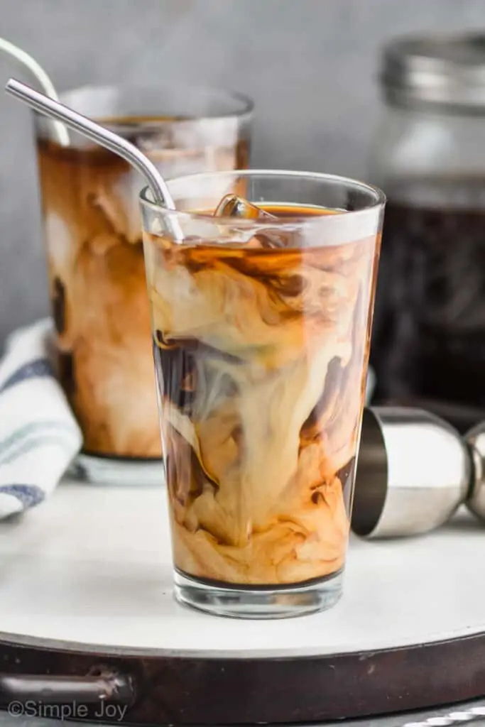 two tall tumblers with ice, iced coffee, and cream swirling in them with metal straws