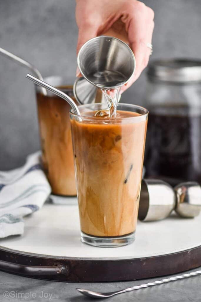 a hand pouring vodka from a metal jigger into a large tumbler full of iced coffee recipe for an iced coffee cocktail