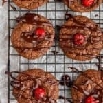 overhead view of several chocolate covered cherry cookies that are on a wire rack and have been drizzled with chocolate ga - 7