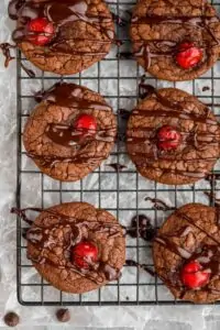 overhead view of several chocolate covered cherry cookies that are on a wire rack and have been drizzled with chocolate ga