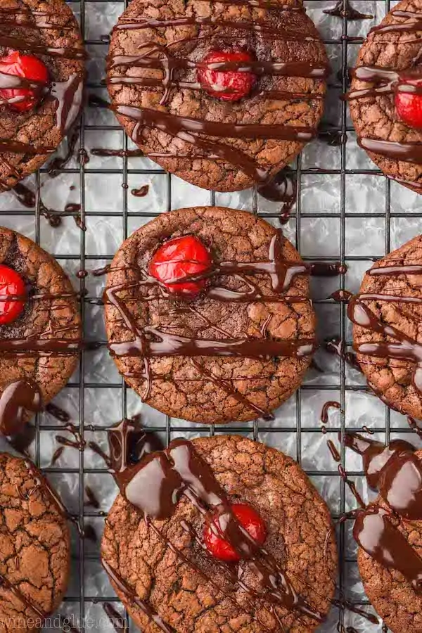 a chocolate covered cherry cookie that has been drizzled with ganache on a wire rack next to other cookies