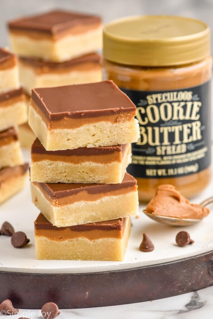 Photo of stacks of Cookie Butter Bars. Jar of cookie butter and a spoon beside stacks of bars.