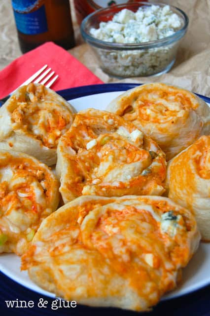 On a white plate, five Buffalo Chicken Pinwheels has cheese and buffalo sauce oozing out. 