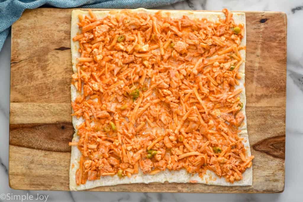 overhead of a square of dough covered in a buffalo sauce, cheese, and chicken mixture