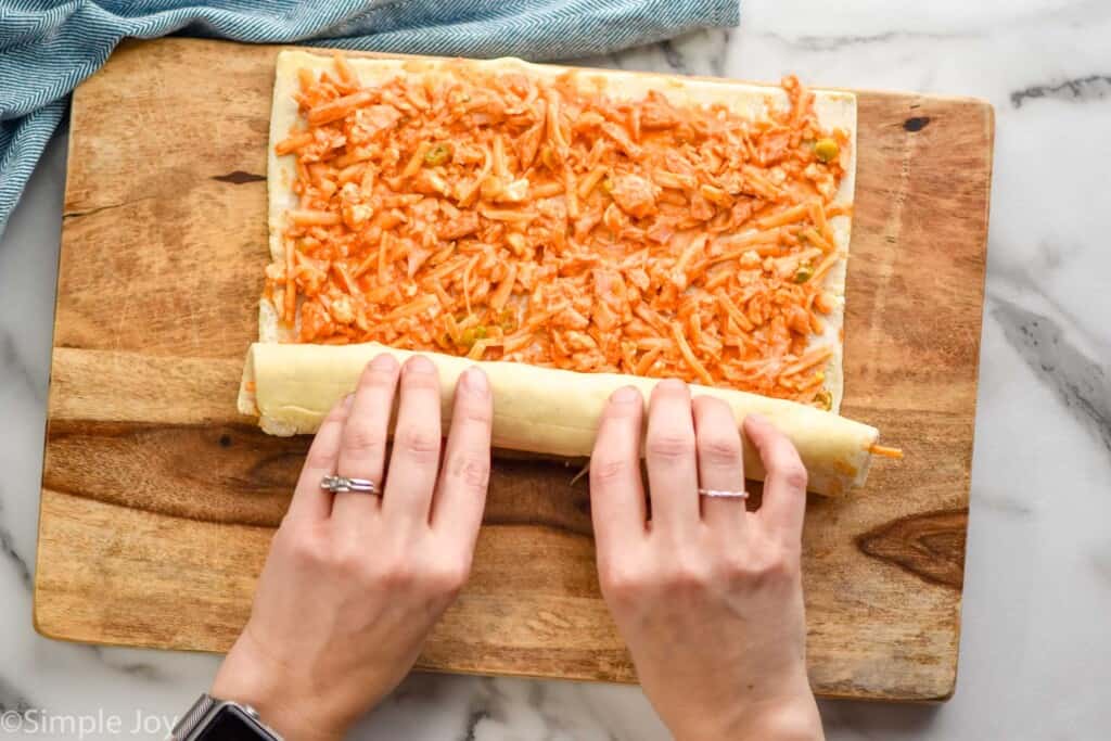 overhead of hands rolling up dough covered in a chicken and buffalo sauce mixture