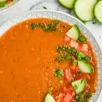 overhead view of a white bowl filled with gazpacho recipe and garnished with chopped fresh vegetables