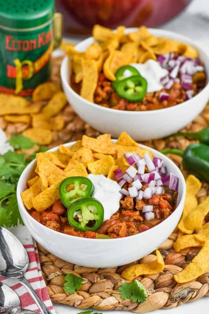 two bowls of ground turkey chili topped with diced red onions, sour cream, jalapenos, and tortilla chips.