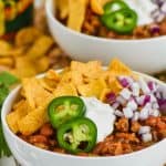 bowl of healthy turkey chili garnished with jalapeños, sour cream, chips and red onions