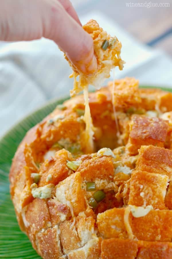 A woman is grabbing a piece of the Buffalo Pull Apart Bread showing the cheese oozy and gooey. 