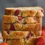 pieces of strawberry banana bread recipe stacked up on a marble cutting board against a dark background