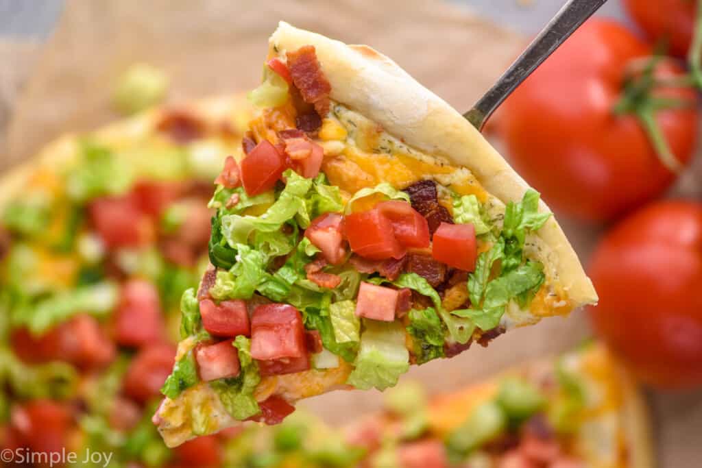 a piece of pizza with bacon lettuce and tomato being lifted up by a spatula