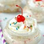 close up of a mason jar with no bake cheesecake, topped with a cherry, whipped cream and sprinkles, says no bake funfetti cheesecake cups - 9
