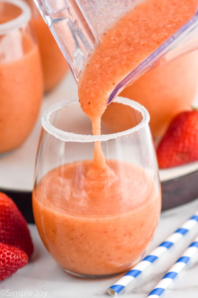 Overhead photo of pitcher of Strawberry Mango Margaritas being poured into a glass with a sugared rim.