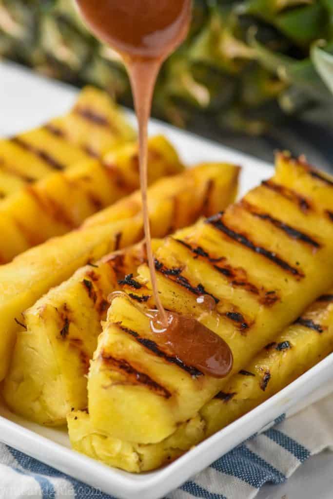 wedges of grilled pineapple on a white plate with cinnamon honey being drizzled over it