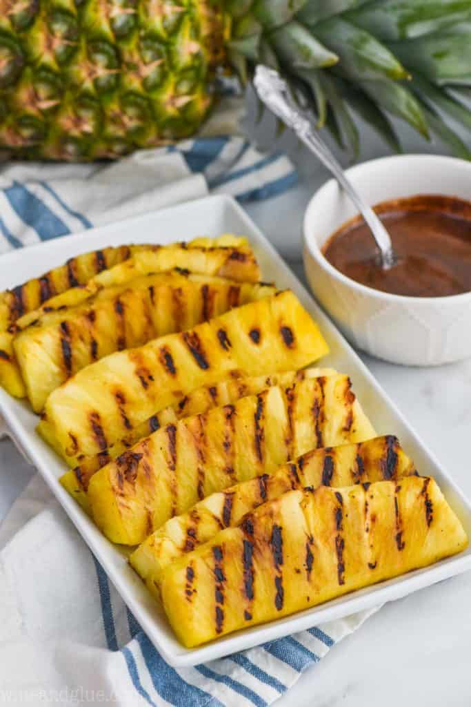 grilled pineapple spears on a platter with a side of the Cinnamon Honey Drizzle