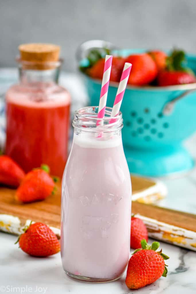 strawberry milk in a small bottle with strawberry syrup in the background