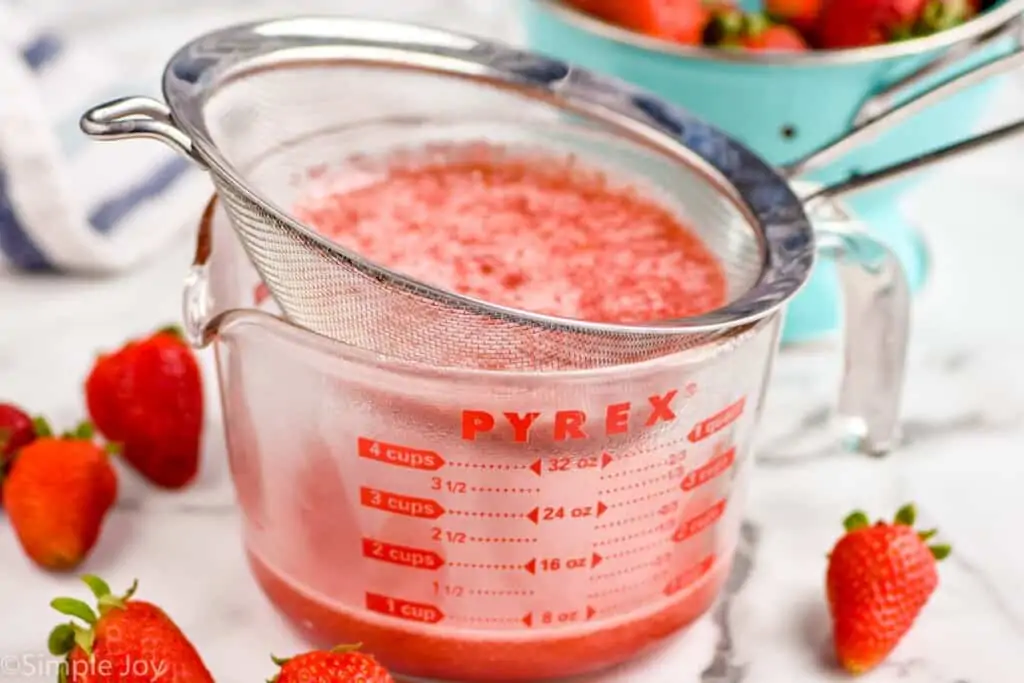 strawberry simple syrup being strained into a measuring cup