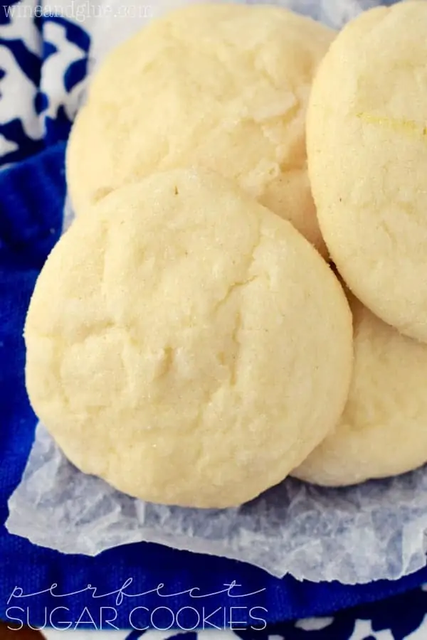 several sugar cookies piled on each other on wax paper which is on a blue cloth napkin
