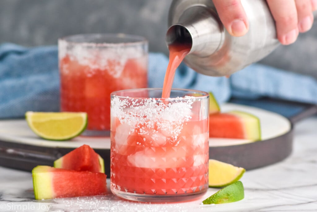 watermelon margarita being poured into a glass that is rimmed with salt