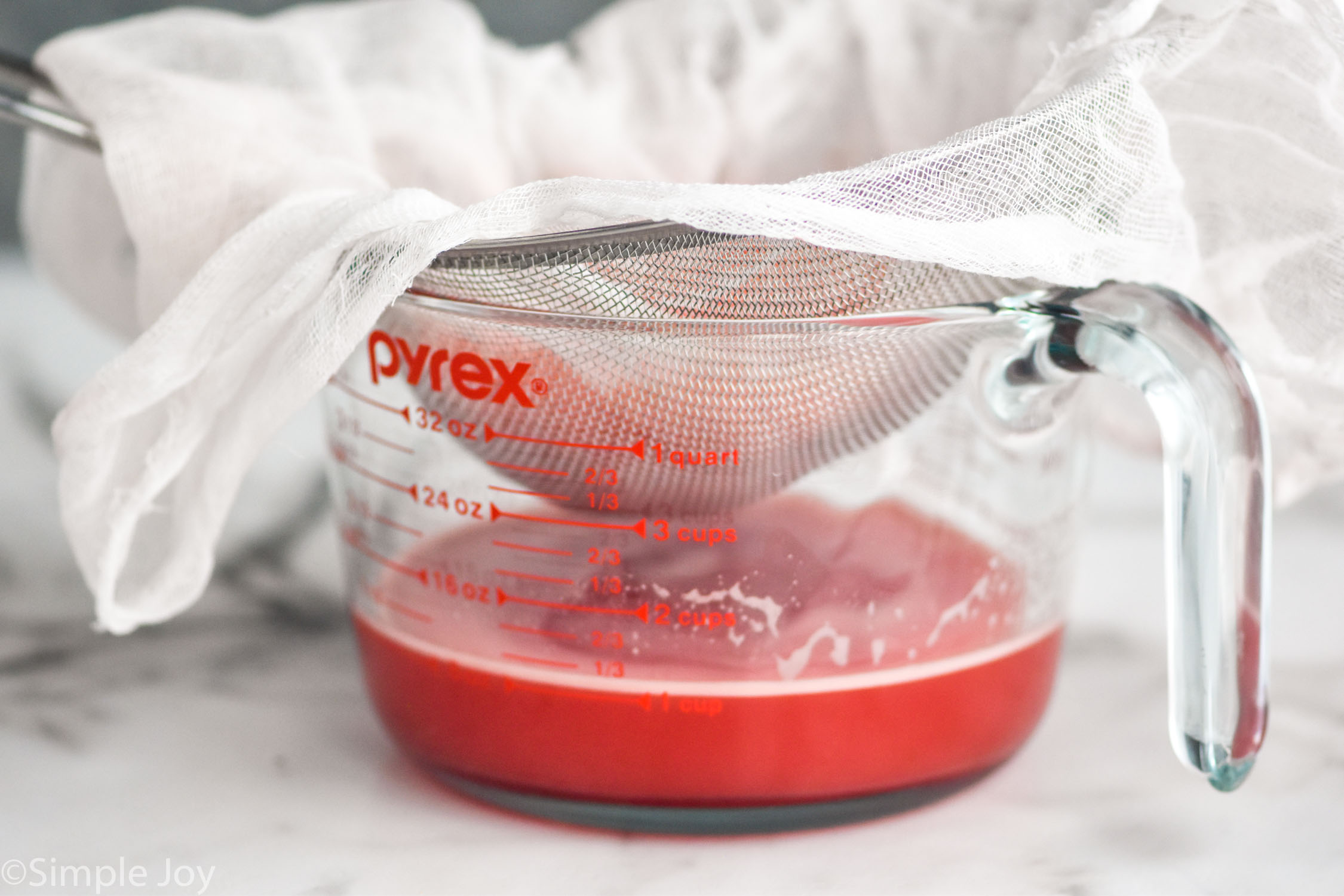 watermelon juice being strained through a wire mesh, lined with cheese cloth, into a measuring cup
