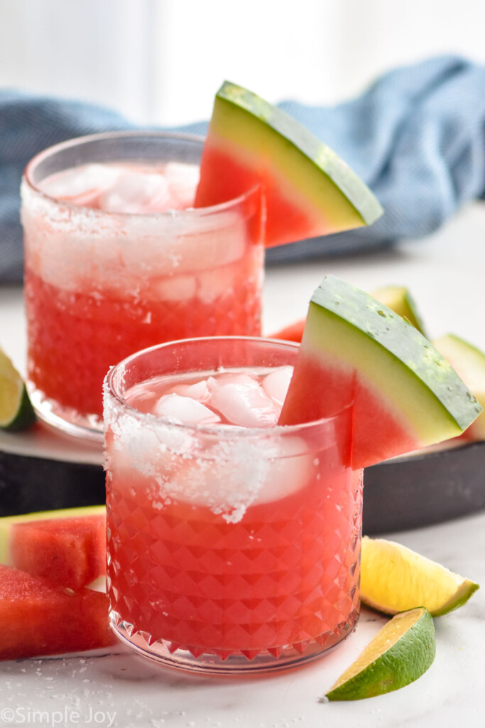 two watermelon margaritas, one on a tray with lime wedges around them