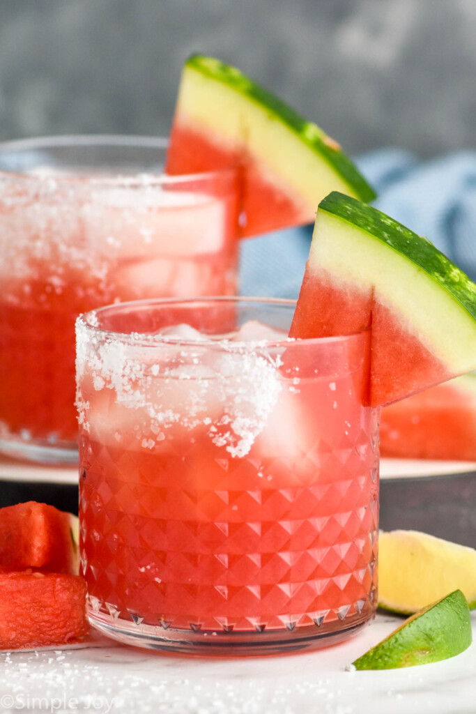 two cups of watermelon margaritas with salt on the rim and a watermelon wedge on the edge
