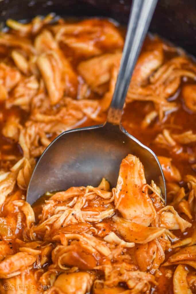 close up of a spoon dishing up bbq pulled chicken in a slow cooker