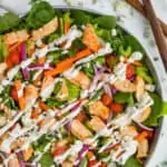 overhead view of a buffalo chicken salad dressed with ranch dressing in a large metal tray with blue cheese, wooden serving utensils, fresh dill, and a red and white napkin around it