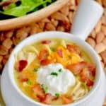 a white soup bowl with chicken bacon ranch soup on a whicker mat with salad in the background