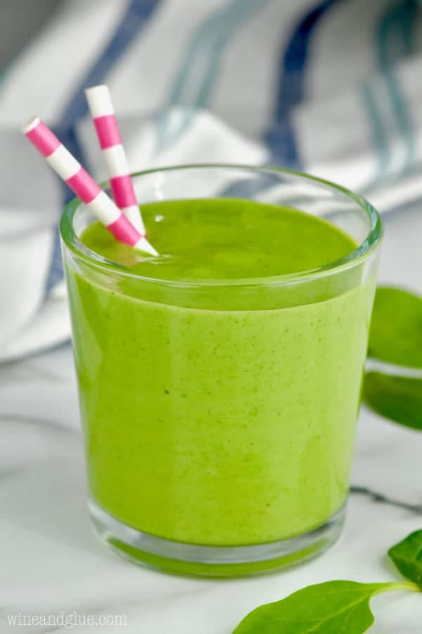 In a glass, the Three Ingredient Green Smoothie has a bright green color with two paper straws. 