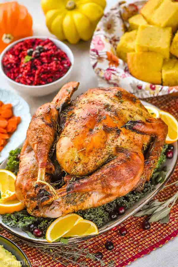 a thanksgiving turkey on a platter with greens, orange wedges, and cranberries