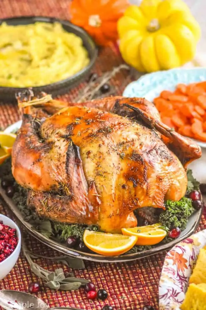 a roast turkey on a platter with greens, orange slices, fresh cranberries, surrounded by side dishes