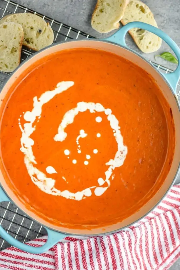 overhead of a tomato bisque recipe that is drizzled with cream in a large stock pot