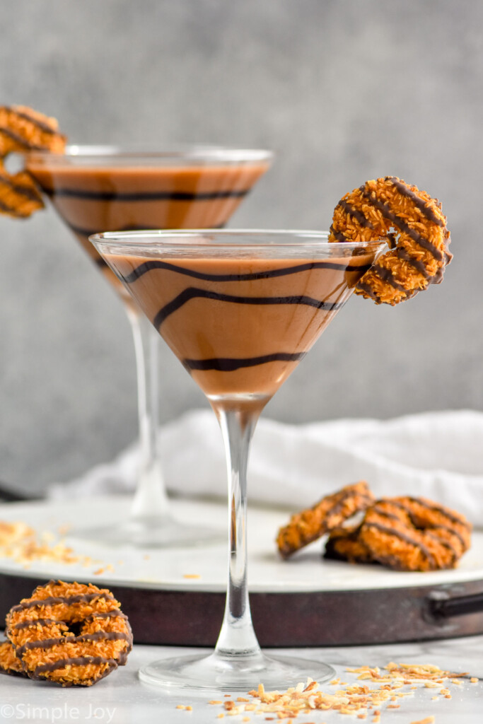 Photo of two Samoa Martinis garnished with Samoa cookies. Extra Samoa cookies on counter beside glasses.