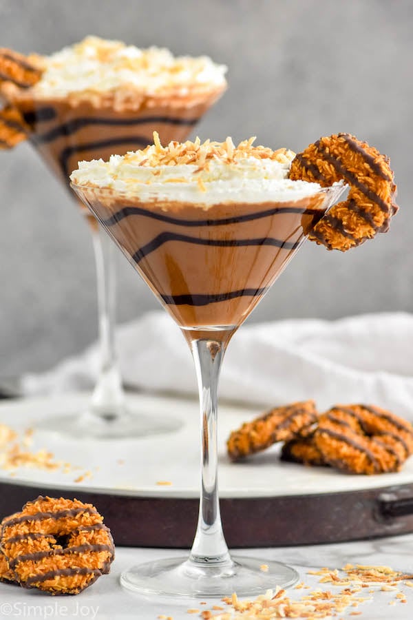 Photo of two Samoa Martinis garnished with Samoa cookies. Extra Samoa cookies on the counter beside Samoa Martinis.