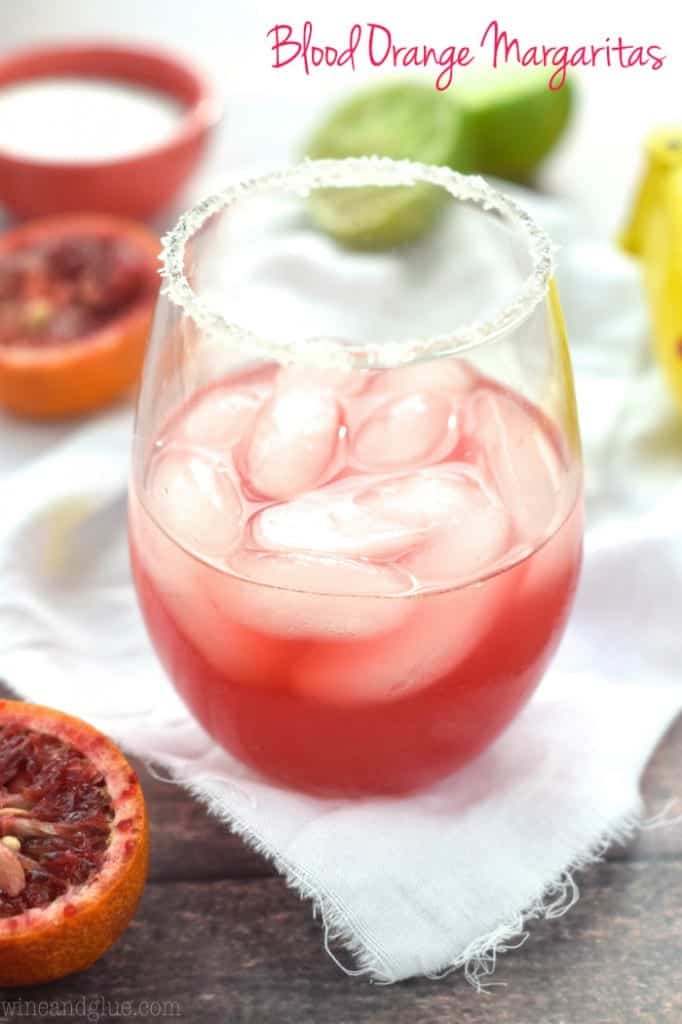 In a glass, the Blood Orange Margaritas has cubed ice in a dark magenta colored drink and rimmed with salt. 