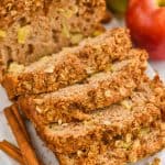 close up of cinnamon apple bread with streusel bread that has been sliced into on a marble cutting board with cinnamon sticks next to it and apples in the background - 11