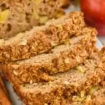 close up of cinnamon apple bread with streusel bread that has been sliced into on a marble cutting board with cinnamon sticks next to it and apples in the background