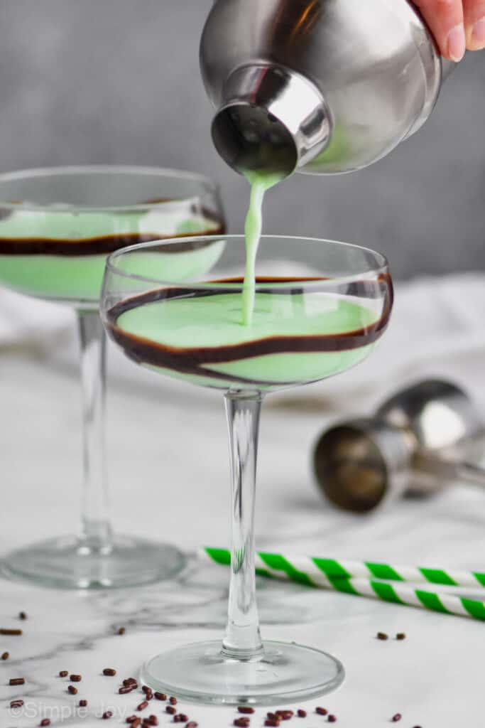 a bright green grasshopper drink recipe being poured into a coupe glass, another in the background