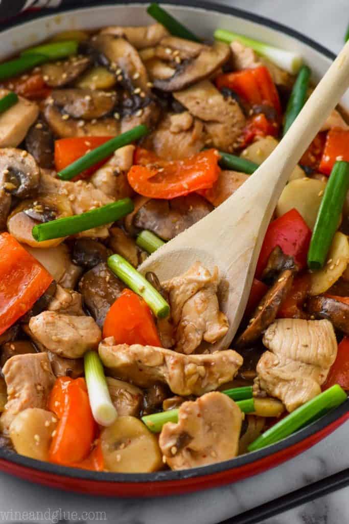 Serving spoon digging into a skillet of easy szechuan chicken garnished with white sesame seeds. 