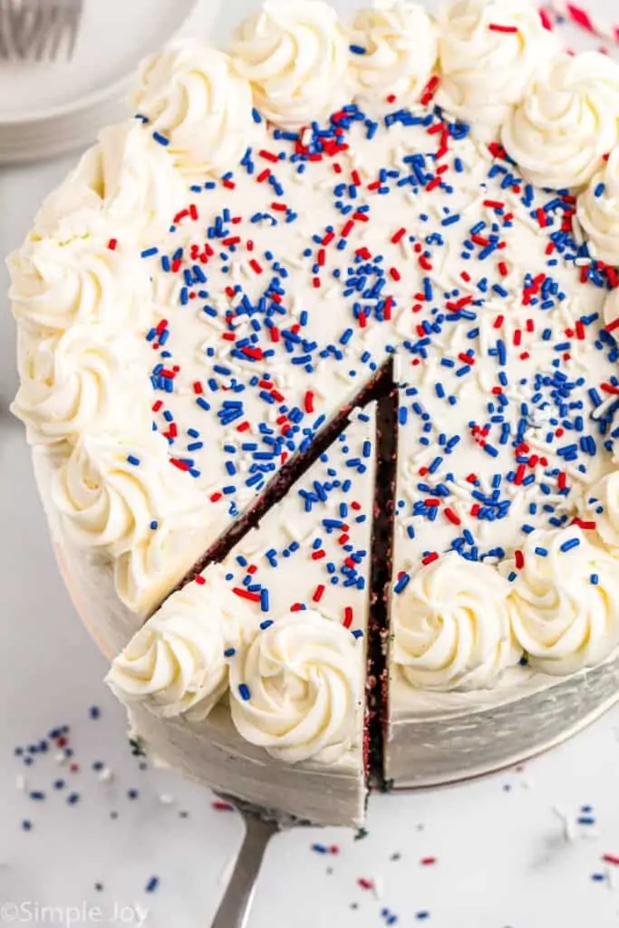 overhead photo of a white cake with red and blue sprinkles and a piece coming out