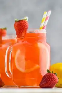 large glass of strawberry lemonade with a strawberry sliced and on the glass as a garnish