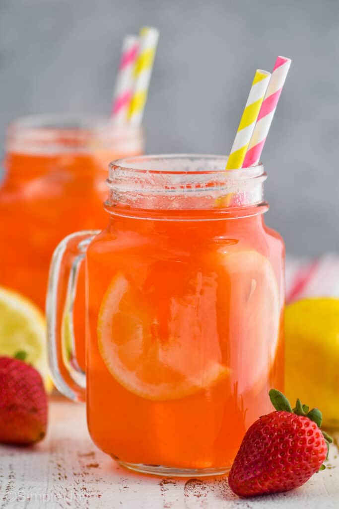 large mason jar glass of strawberry lemonade with lemon slides inside the drink and served with paper straws