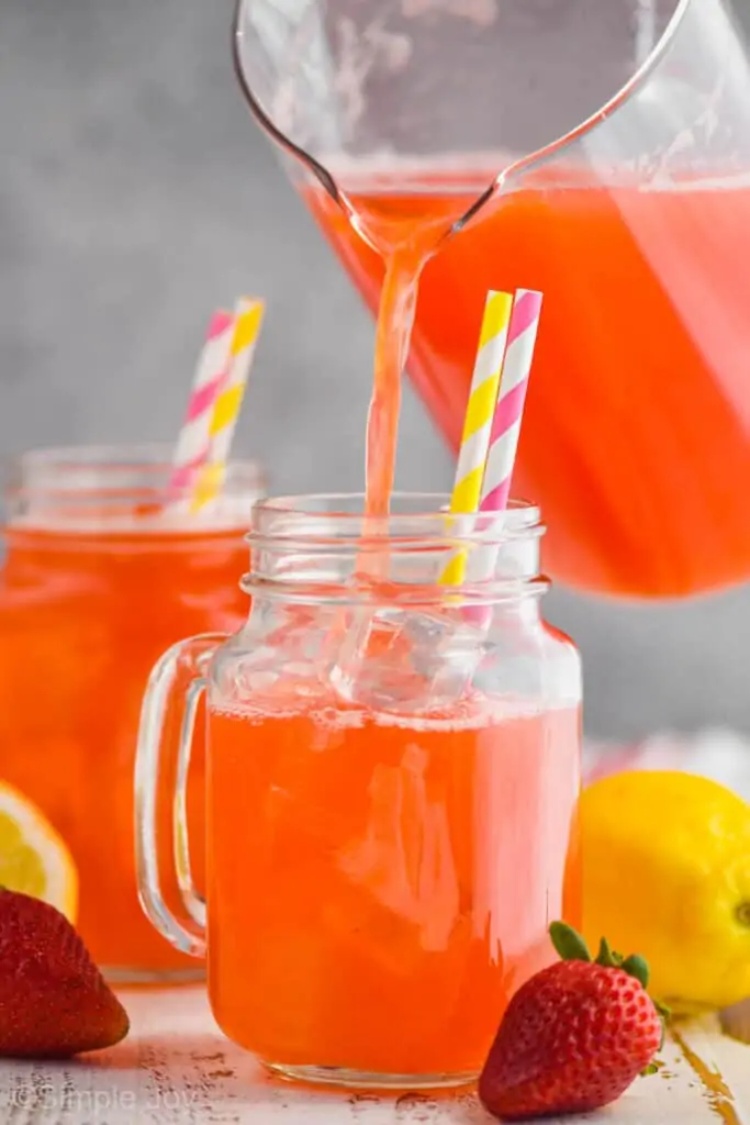 pitcher pouring strawberry lemonade recipe into a large glass mug