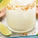 pinterest graphic of close up of a coconut margarita in a glass rimmed with toasted coconut and garnished with a lime wedge
