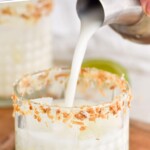 pinterest graphic of coconut margaritas recipe being poured into a tumbler rimmed with toasted coconut