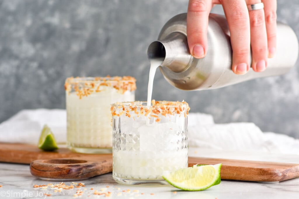 coconut lime margarita being poured from a shaker into a prepared tumbler