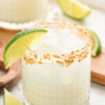 close up of a coconut margarita in a glass rimmed with toasted coconut and garnished with a lime wedge